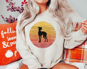May include: A beige sweatshirt with a vintage-style graphic of a black silhouette of an Italian Greyhound dog standing in front of a sunset. The graphic is in a circle with a distressed, faded look.