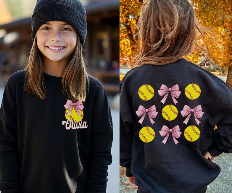 May include: Black sweatshirt with a softball and bow design on the front and multiple softball and bow designs on the back. The text "Olivia" is on the front of the sweatshirt.