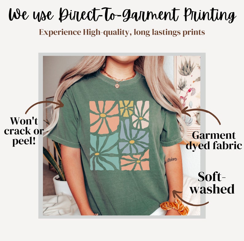 Op de afbeelding: Een groen T-shirt met een bloemenprint. Het shirt is gemaakt van een zachte, garment-geverfde stof en is zacht gewassen. De tekst "We use Direct-To-garment Printing" staat bovenaan de afbeelding. De tekst "Experience High-quality, long lasting prints" staat onder de eerste regel tekst. De tekst "Won't crack or peel!" staat aan de linkerkant van de afbeelding. De tekst "Garment dyed fabric" staat aan de rechterkant van de afbeelding. De tekst "Soft-washed" staat aan de rechterkant van de afbeelding.