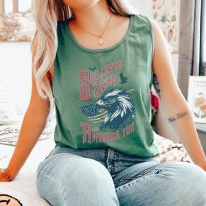 May include: A green tank top with a graphic print of an eagle and the text "She Loves Jesus and America Too".