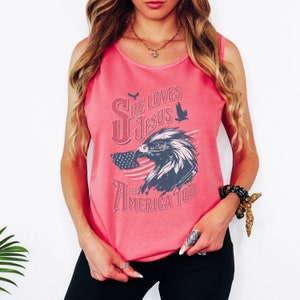May include: Pink tank top with a graphic of an eagle and an American flag. The text on the shirt reads "She Loves Jesus and America Too."