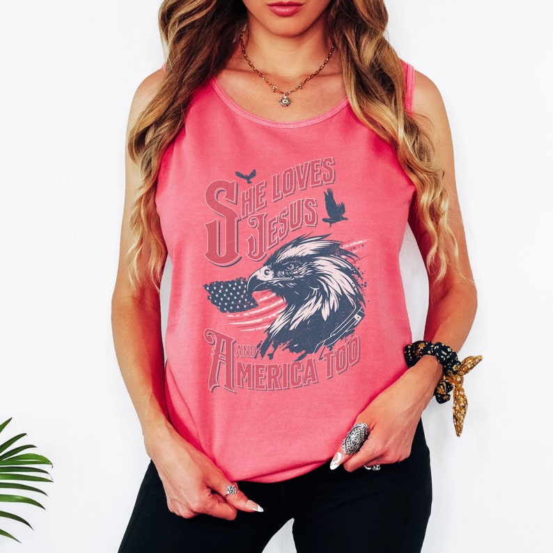 May include: Pink tank top with a graphic of an eagle and an American flag. The text on the shirt reads "She Loves Jesus and America Too."