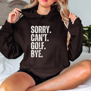 May include: A black hoodie with a white distressed graphic that reads "SORRY. CAN'T. GOLF. BYE."
