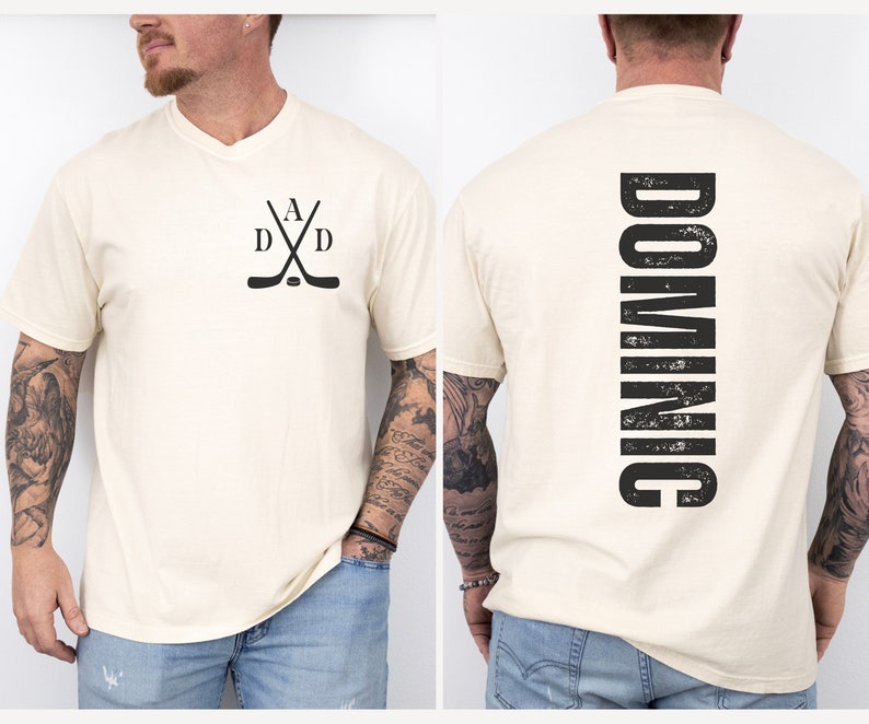 Puede incluir: Una camiseta blanca con un dise&ntilde;o de palo de hockey negro en la parte delantera y la palabra "DOMINIC" impresa verticalmente en la parte posterior.