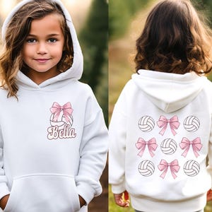 May include: White hooded sweatshirt with a volleyball and pink bow design. The text "Bella" is printed on the front of the sweatshirt.