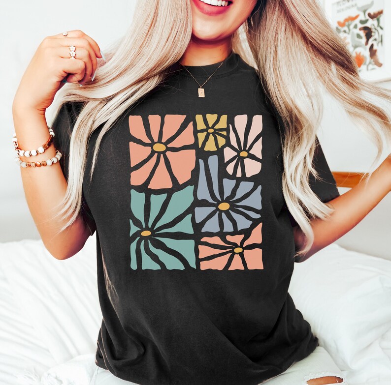 Op de afbeelding: Een zwart T-shirt met een grafisch ontwerp van kleurrijke abstracte bloemen. De bloemen zijn in een vierkant patroon gerangschikt en hebben een retro-stijl.