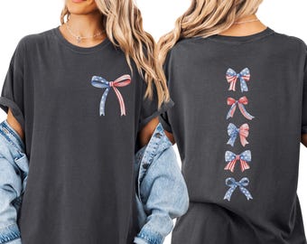 May include: A charcoal gray short-sleeve t-shirt featuring a single bow graphic with red, white, and blue star and stripe patterns on the front chest and a vertical column of five similar patriotic bows printed on the back.