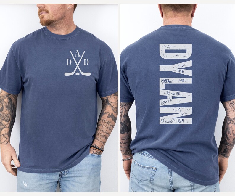 Puede incluir: Una camiseta azul con un dise&ntilde;o de palo de hockey blanco en la parte delantera y la palabra "DYLAN" en blanco en la parte posterior.