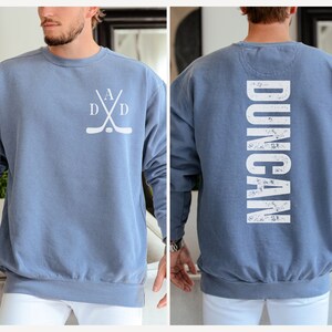 Puede incluir: Una sudadera azul con un dise&ntilde;o de palo de hockey blanco en la parte delantera y la palabra "DUNCAN" en blanco en la parte posterior.