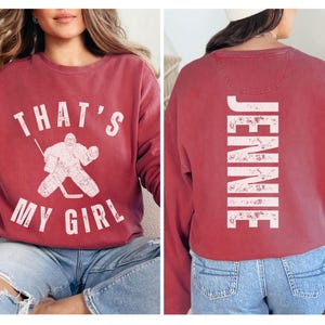 May include: Two red sweatshirts with white text. One sweatshirt says "That's My Girl" with a hockey player graphic. The other sweatshirt says "Jennie".