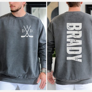 Puede incluir: Una sudadera gris con un dise&ntilde;o de palo de hockey blanco en la parte delantera y el nombre "BRADY" en blanco en la parte posterior.