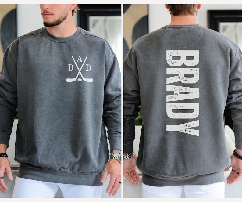 Puede incluir: Una sudadera gris con un dise&ntilde;o de palo de hockey blanco en la parte delantera y el nombre "BRADY" en blanco en la parte posterior.