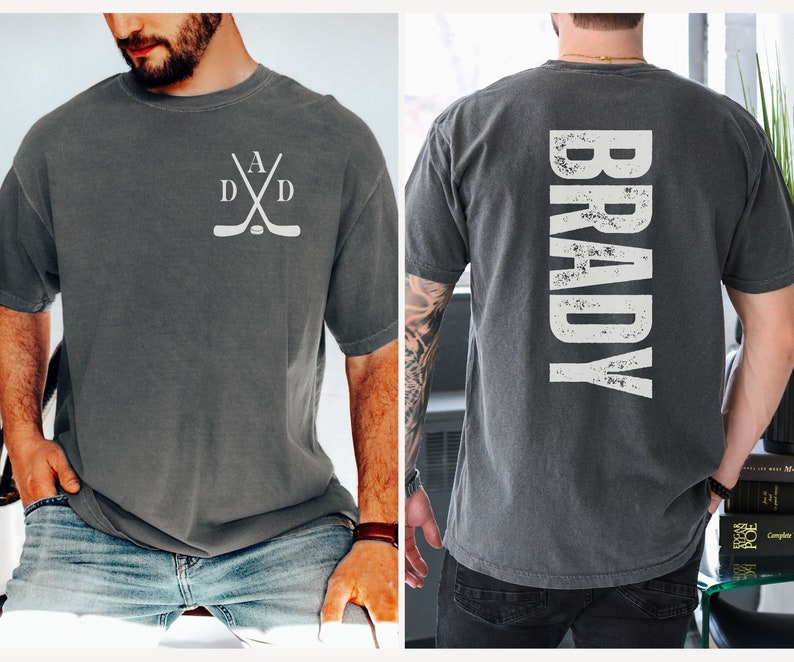 Puede incluir: Una camiseta gris con un dise&ntilde;o de palo de hockey blanco en la parte delantera y la palabra "BRADY" en letras blancas desgastadas en la parte trasera.