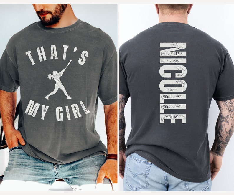 May include: Two gray t-shirts with white text and graphics. The front shirt says "That's My Girl" with a silhouette of a woman swinging a baseball bat. The back shirt says "Nicole" in a distressed font.