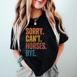 May include: A black t-shirt with a vintage-style graphic that reads "SORRY. CAN'T. HORSES. BYE."