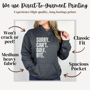 May include: A dark gray hooded sweatshirt with a white graphic print that reads "SORRY. CAN'T. GOLF. BYE." The sweatshirt has a spacious pocket and a classic fit. The text "Won't crack or peel!" and "Medium heavy fabric" are written on the left side of the image. The text "Classic Fit" and "Spacious Pocket" are written on the right side of the image.