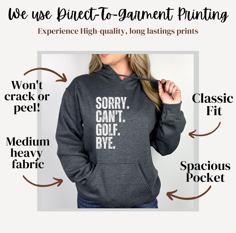 May include: A dark gray hooded sweatshirt with a white graphic print that reads "SORRY. CAN'T. GOLF. BYE." The sweatshirt has a spacious pocket and a classic fit. The text "Won't crack or peel!" and "Medium heavy fabric" are written on the left side of the image. The text "Classic Fit" and "Spacious Pocket" are written on the right side of the image.