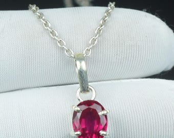 May include: A silver pendant necklace with a vivid, oval-cut ruby gemstone. The ruby is a deep red hue, secured by four silver prongs. The chain is a delicate silver link style.