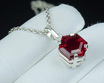 May include: A silver necklace featuring a faceted, hexagonal, deep red gemstone pendant. The pendant is set in a silver frame and hangs from a delicate silver chain. The background is a dark, solid color.