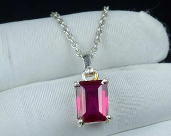 May include: A silver necklace featuring a rectangular, deep red gemstone pendant. The pendant is set in a silver frame and hangs from a delicate silver chain. The gemstone has a vibrant, polished appearance, set against a black background.