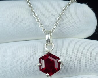 May include: A silver necklace featuring a hexagonal, deep red gemstone pendant. The pendant is set with small silver prongs at each corner. The chain is delicate and the pendant is displayed against a white background.