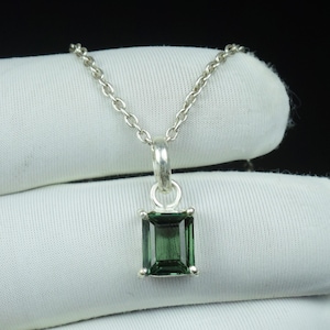 Puede incluir: Un collar de plata con un colgante rectangular de piedra preciosa verde esmeralda. El colgante está engastado en un bisel de plata y cuelga de una delicada cadena. La piedra preciosa tiene un color profundo y rico.