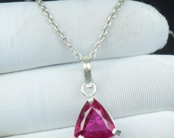 Pode incluir: Um colar de prata com um pingente triangular de gema magenta. O pingente é fixado em uma moldura de prata e pendurado em uma delicada corrente de prata. A gema tem uma superfície facetada. O colar é exibido em uma superfície branca.