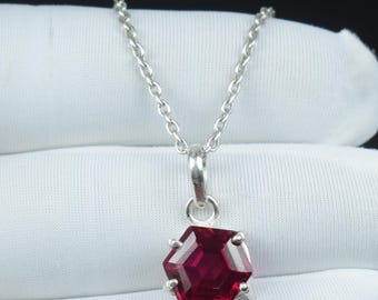 May include: A silver necklace with a hexagonal, deep red gemstone pendant. The pendant is faceted, catching the light and displaying a rich, vibrant color. The chain is delicate and the pendant is the focal point.