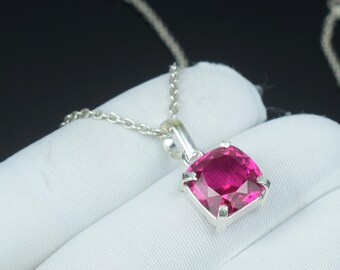 May include: A silver necklace featuring a square, vibrant pink gemstone pendant. The pendant is set in a silver frame and hangs from a delicate silver chain. The gemstone has multiple facets, reflecting light. The necklace is displayed on a white surface.