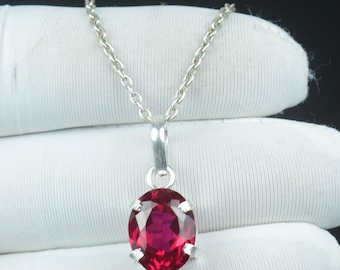 May include: A silver necklace with a vibrant red oval gemstone pendant. The gemstone is set in a silver bezel and hangs from a delicate silver chain. The pendant is approximately 0.75 inches in length.
