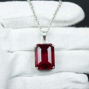 May include: A silver necklace featuring a rectangular, deep red gemstone pendant. The pendant is set in a silver frame and hangs from a delicate silver chain. The gemstone has a faceted cut, reflecting light.