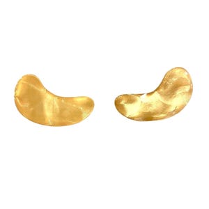 May include: Two gold under eye patches, shaped like crescent moons, are shown against a white background.