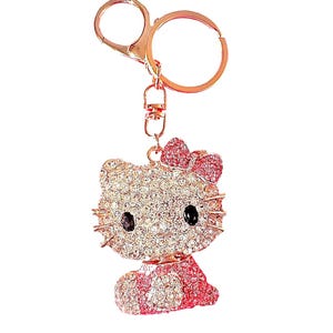 Può includere: Un portachiavi dorato con un design Hello Kitty rosa e bianco con strass. Il portachiavi ha un anello di metallo e un moschettone.