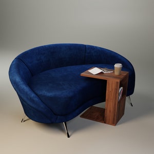 May include: A blue velvet curved sofa with a wooden side table. The table has a shelf and a magazine on top. A disposable coffee cup is on the table.