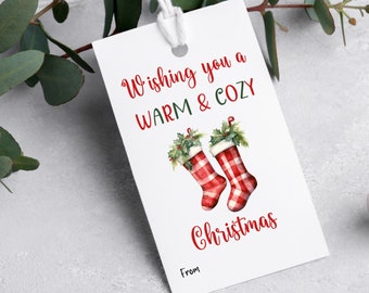 Könnte beinhalten: Weißer Geschenkanhänger mit roten und grünen Aquarell-Illustrationen von Weihnachtsstrümpfen. Der Anhänger trägt den Text "Wishing you a warm & cozy Christmas" und hat einen Platz zum Schreiben von "From".