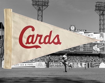 Puede incluir: Un banderín vintage en crema con la palabra "Cards" en rojo. El banderín está frente a una escena de juego de béisbol en blanco y negro, con jugadores en el campo y una multitud en las gradas. El fondo es en blanco y negro.