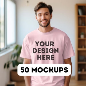 May include: A man wearing a pink t-shirt with the text "YOUR DESIGN HERE" printed on the front. The text "50 MOCKUPS" is printed on a white rectangle below the shirt.