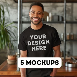 以下が含まれることがあります： 「YOUR DESIGN HERE」という文字が書かれた黒いTシャツのモックアップ。Tシャツは笑顔の人物が着用しています。背景はぼやけたキッチンです。