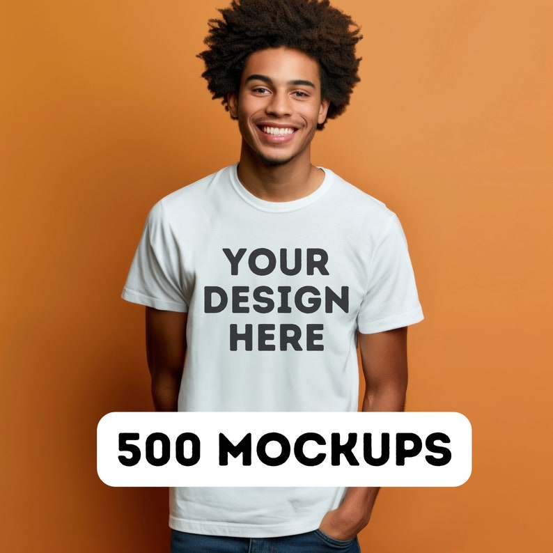以下が含まれることがあります： 白いTシャツに「YOUR DESIGN HERE」という文字が前面に印刷されています。Tシャツは、オレンジ色の背景に、縮れた髪の毛の人によって着用されています。500 MOCKUPS.