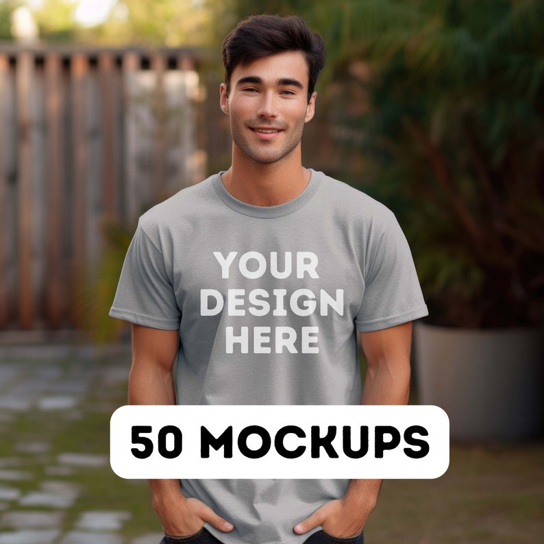 May include: A man wearing a gray t-shirt with the text "YOUR DESIGN HERE" printed on the front. The text is in white. The man is standing in front of a wooden fence and green plants. The image is a mockup for a t-shirt design.