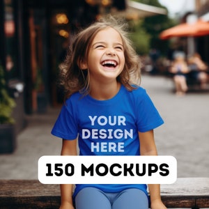 May include: A young girl wearing a blue t-shirt with the text "YOUR DESIGN HERE" printed on the front. She is smiling and looking up.