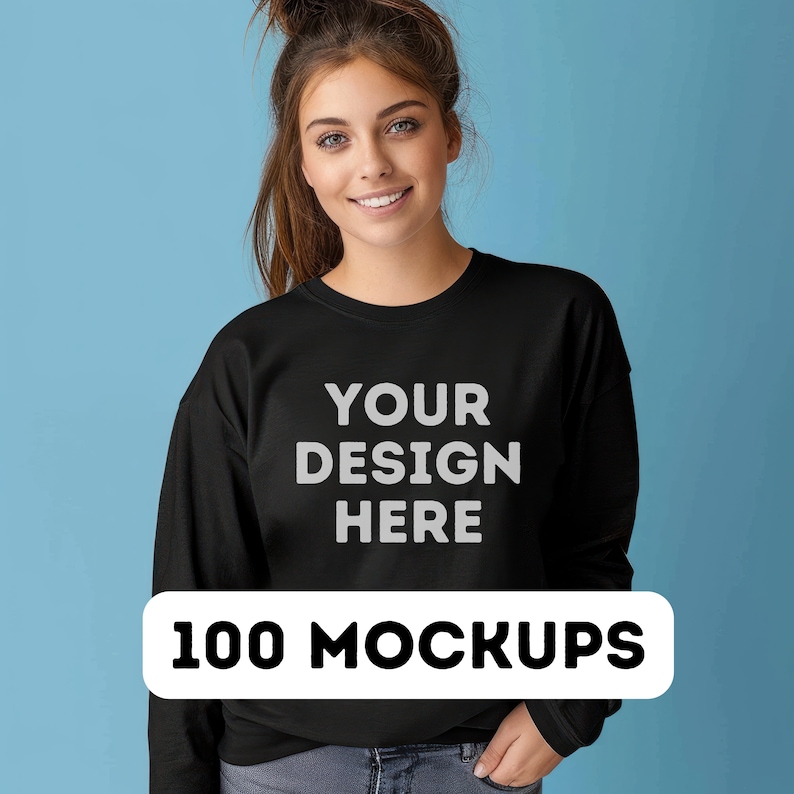 May include: A black sweatshirt with the text "YOUR DESIGN HERE" printed on the front. The text is in a light gray color. The sweatshirt is being modeled by a person with long brown hair. The background is a light blue color. 100 MOCKUPS.
