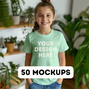 May include: A young person wearing a light green t-shirt with the text "YOUR DESIGN HERE" in white. A banner at the bottom reads "50 MOCKUPS". The background includes plants and shelves.