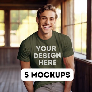 以下が含まれることがあります： 男性が、前面に「YOUR DESIGN HERE」という文字が印刷された緑色のTシャツを着ています。文字は白で、Tシャツの中央に配置されています。男性は笑顔でカメラを見ています。5 MOCKUPSは、黒い長方形に白い文字で書かれています。