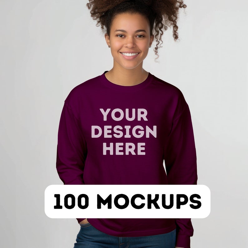 May include: A maroon sweatshirt with the text "YOUR DESIGN HERE" printed on the front. The sweatshirt is being modeled by a person with curly hair. 100 MOCKUPS.
