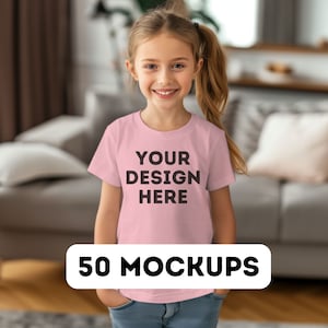 May include: A young girl wearing a light pink t-shirt with the text "YOUR DESIGN HERE" in black. The image also includes a white banner at the bottom with the text "50 MOCKUPS". The girl is smiling and has her hands in her pockets.
