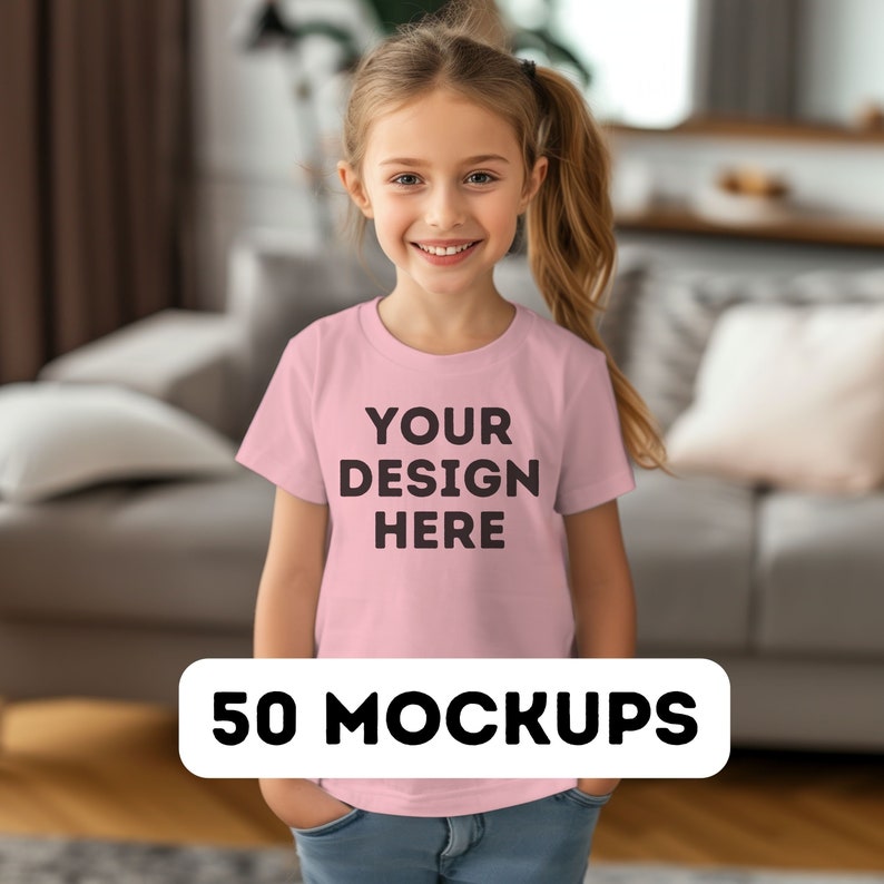 May include: A young girl wearing a light pink t-shirt with the text "YOUR DESIGN HERE" in black. The image also includes a white banner at the bottom with the text "50 MOCKUPS". The girl is smiling and has her hands in her pockets.