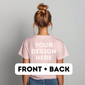 以下が含まれることがあります： 背面に「YOUR DESIGN HERE」という文字が印刷されたピンクのTシャツ。カメラに向かって背を向けている人が着ています。