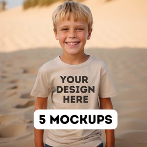 May include: A young person wearing a beige t-shirt with the text "YOUR DESIGN HERE" printed on the front. The t-shirt is a mockup for a design project. The person is standing in front of a sandy background. 5 MOCKUPS is written in a white rectangle at the bottom of the image.