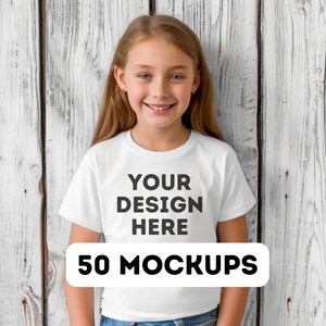 May include: A young girl wearing a white t-shirt with the text "YOUR DESIGN HERE" in black. Below the text is a white rectangle with the words "50 MOCKUPS" in black. The background is a white wooden wall.
